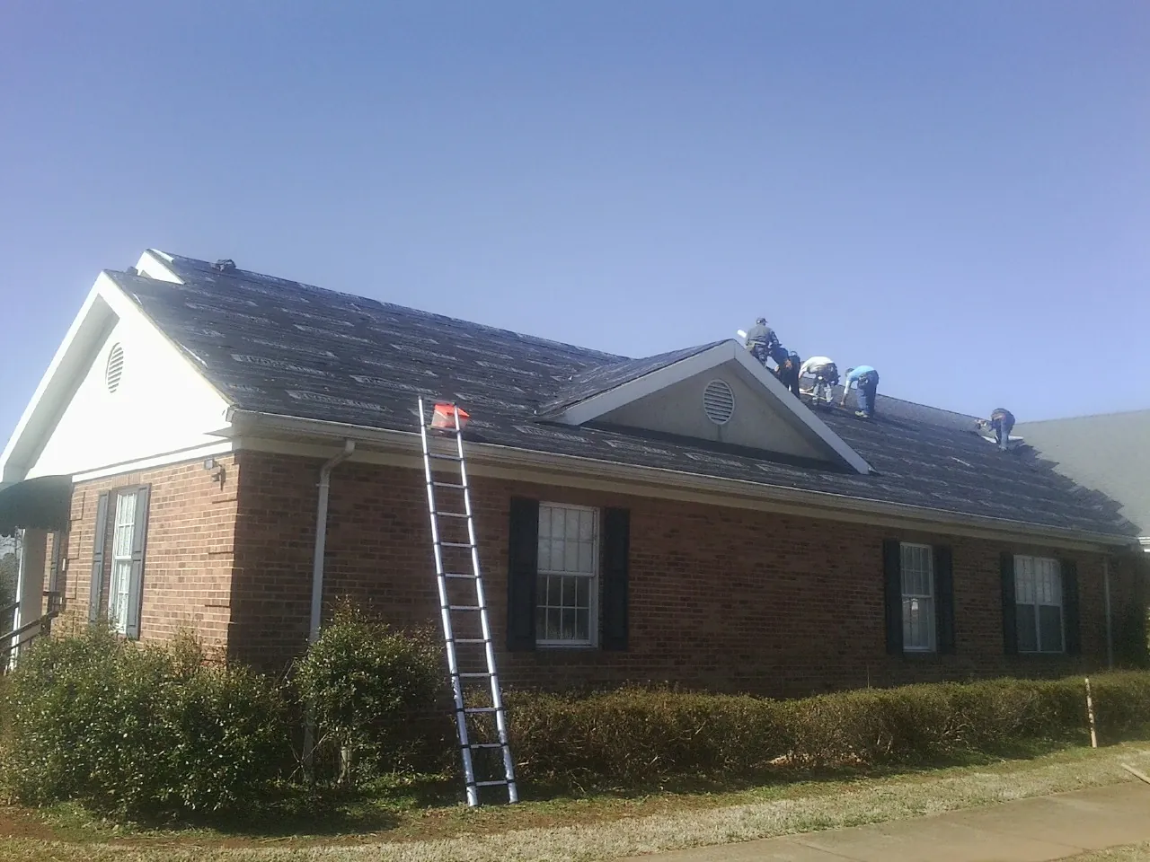 Crew tearing shingles off a brick ranch roof with a ladder set — Metal Roof Repair work by our crew in Altoona